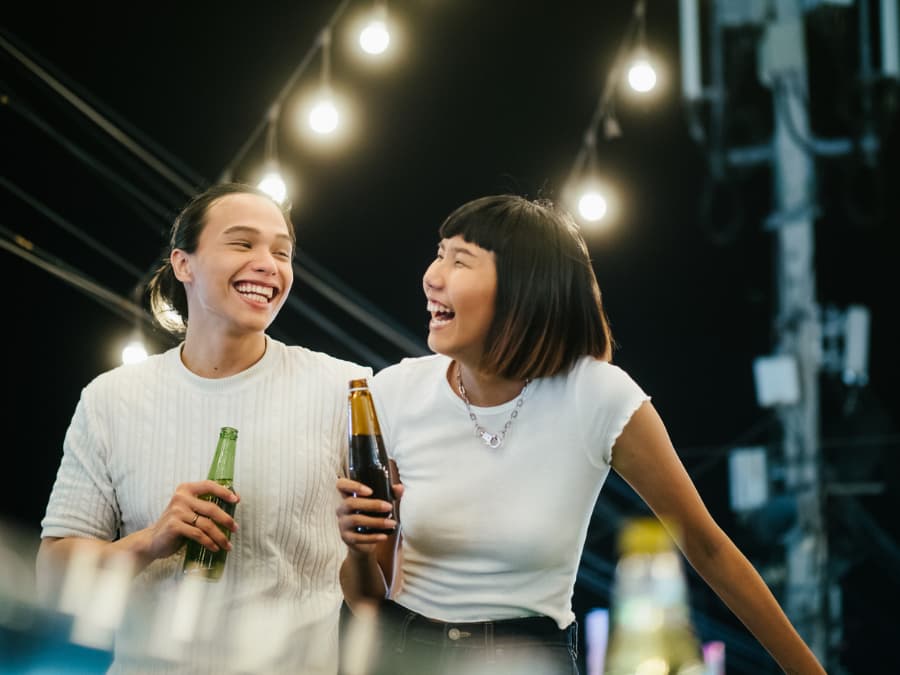 A couple laughs on rooftop location while holding bottles of gluten-free beer