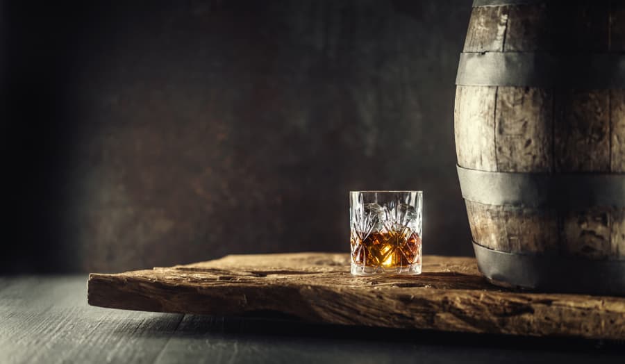 Bourbon in a glass next to a wood barrel.