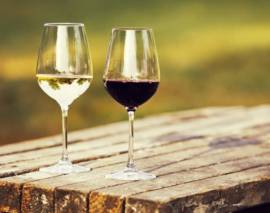 Glass of white wine and glass of red wine side by side on rustic wood table