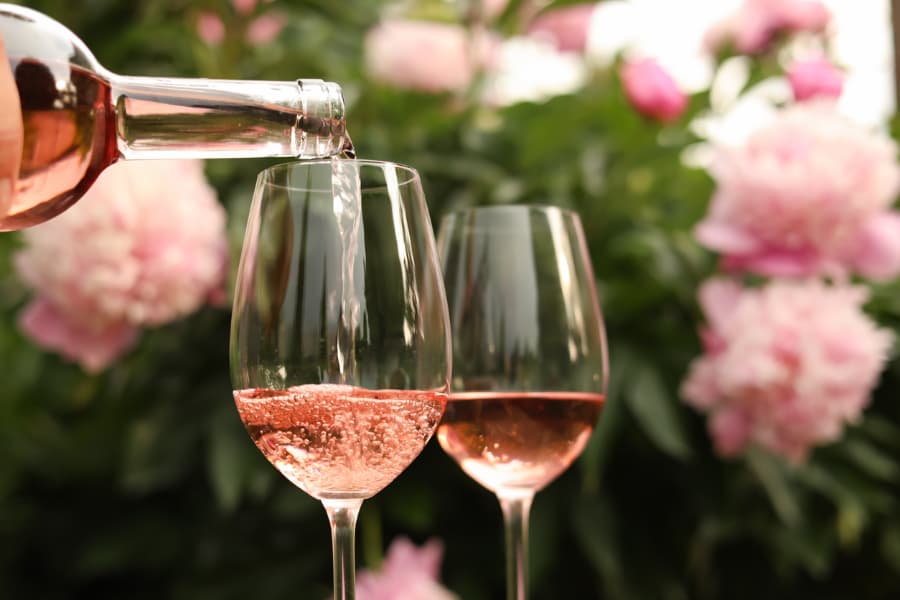 Pouring non-alcoholic rose wine into two glasses with pink flowers in background