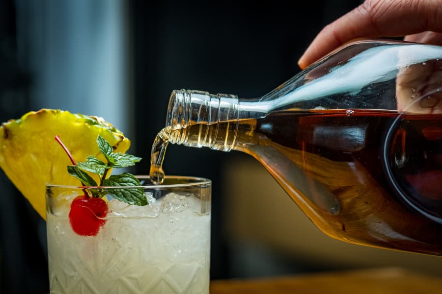 Bartender pouring rum into a tropical drink with fruit garnish