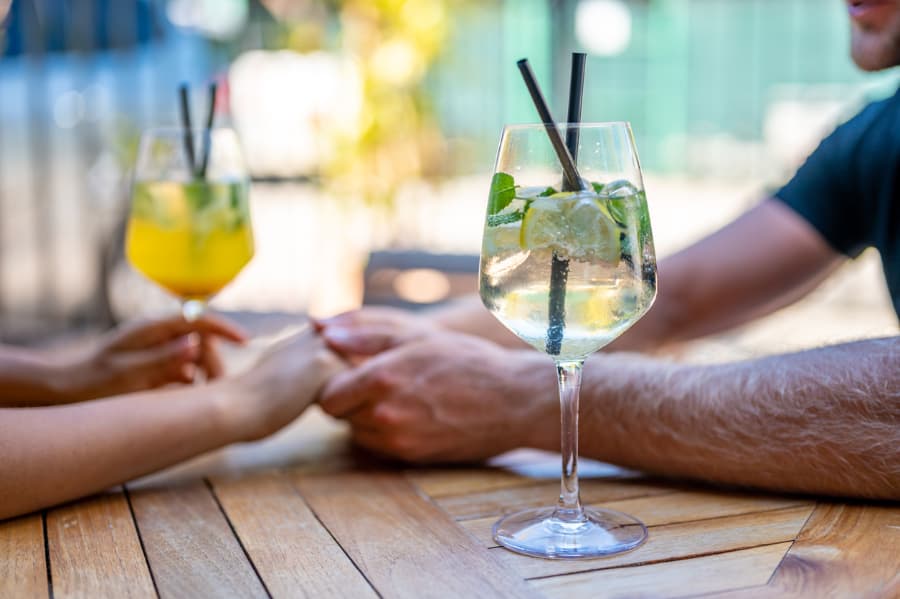 Couple with two gin and tonics sitting on bar tabletop hold hands