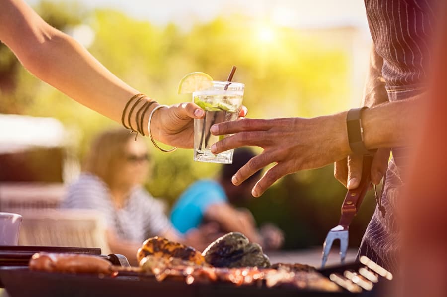 Partygoers sharing cocktail by the grill at summer party 