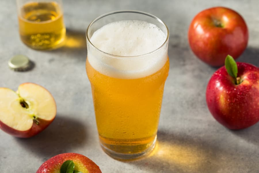 Pint glass of refreshing cold hard apple cider on bar top surrounded by apples