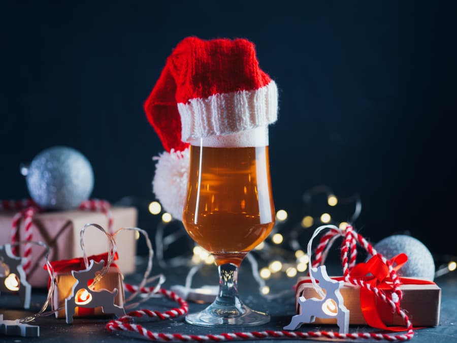 Tall glass of light beer in Santa Claus hat on holiday party table